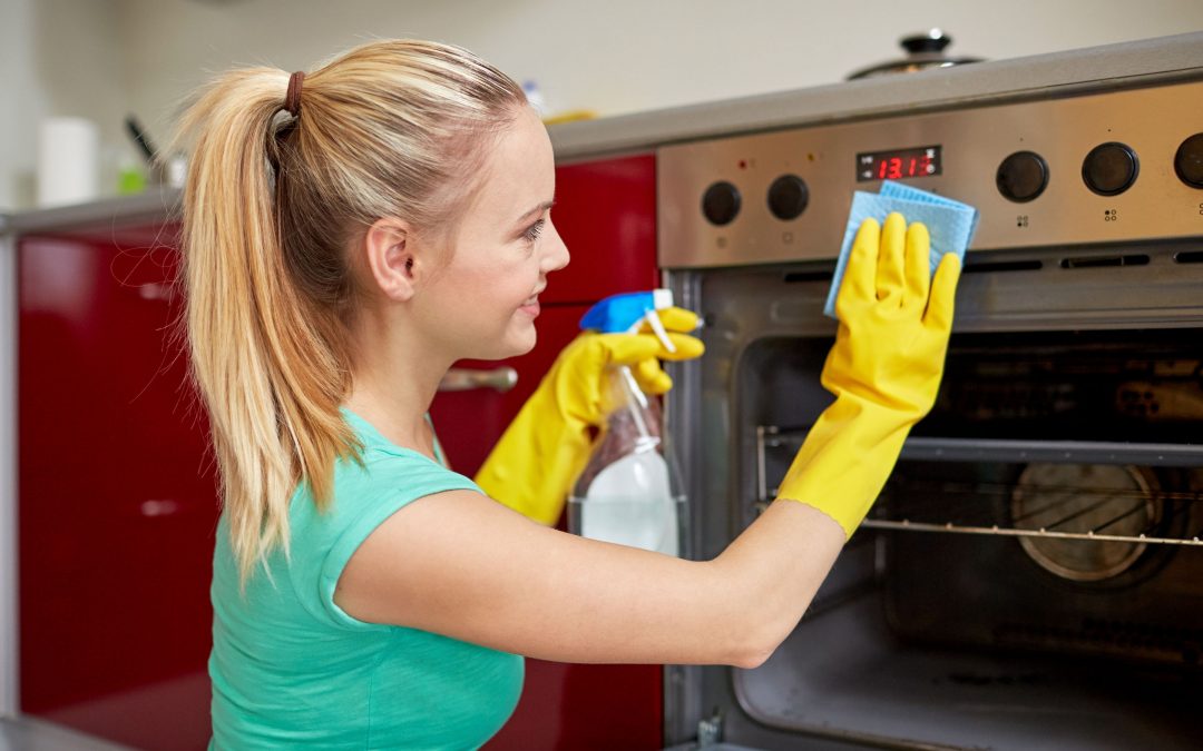 Menschen, Hausarbeit und Hauswirtschaft Konzept - glückliche Frau mit Flasche Spray Reinigungsmittel Reinigungsofen zu Hause Küche